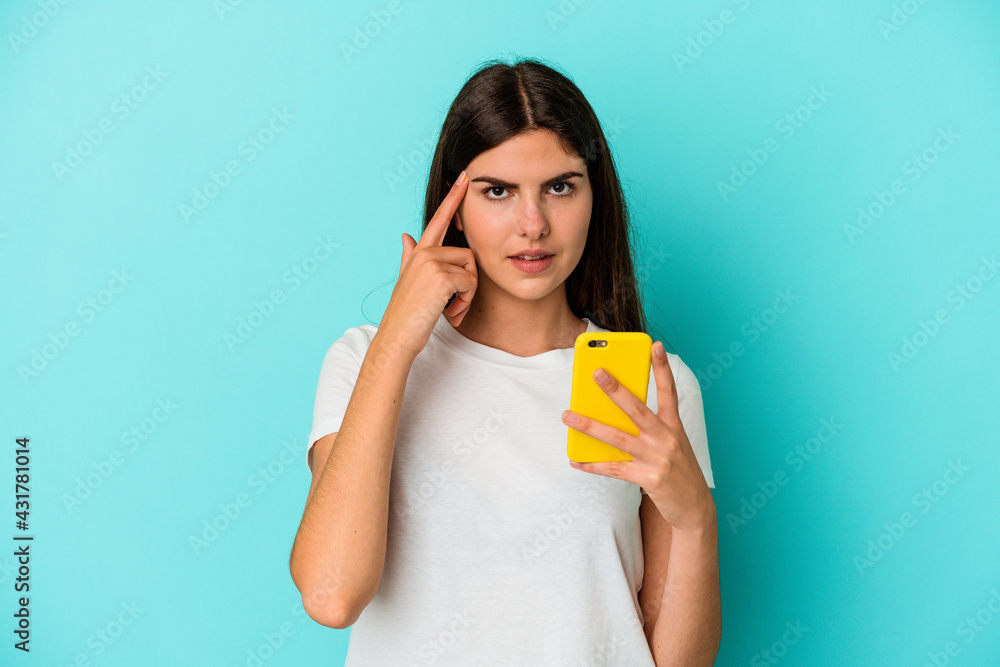 Young caucasian woman holding a mobile phone isolated on blue background pointing temple with finger, thinking, focused on a task. Young caucasian woman holding a mobile phone isolated on blue background pointing temple with finger, thinking, focused on a task.