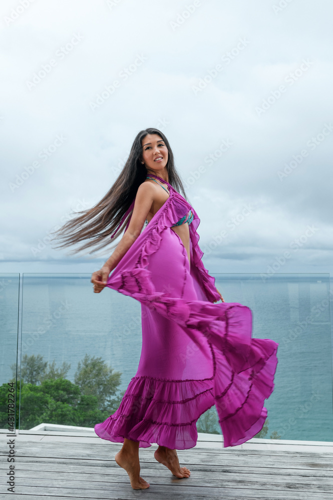 Playful woman a in a purple cape posing while standing on the terrace against the backdrop of the seascape Playful woman a in a purple cape posing while standing on the terrace against the backdrop of the seascape