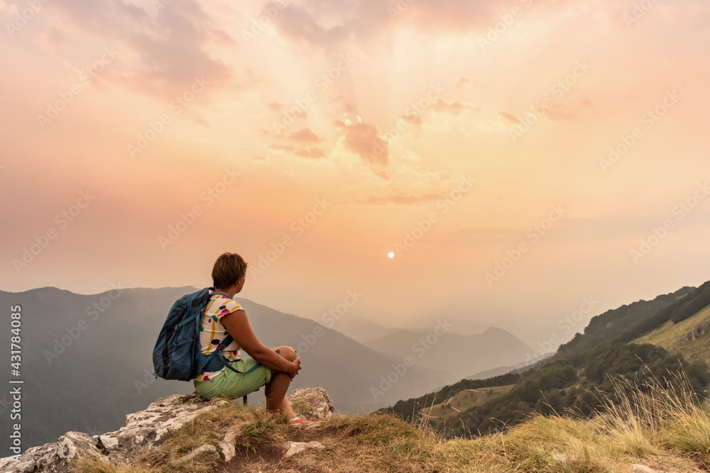 One tourist with backpacks enjoying sunset on top of a mountain One tourist with backpacks enjoying sunset on top of a mountain