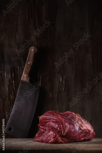 Billede på lærred large piece of raw beef tenderloin lezhin on a cutting board with a kitchen cleaver on the background of an old wooden wall