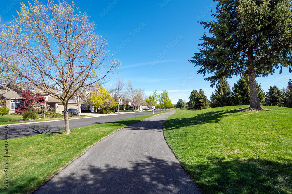 A suburban street of homes in a subdivision across from a park and walking trail path in the town of Coeur d'Alene, Idaho, USA