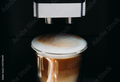 Glass transparent cup of fresh cappuccino with froth in the coffee maker. Close-up. Copy space