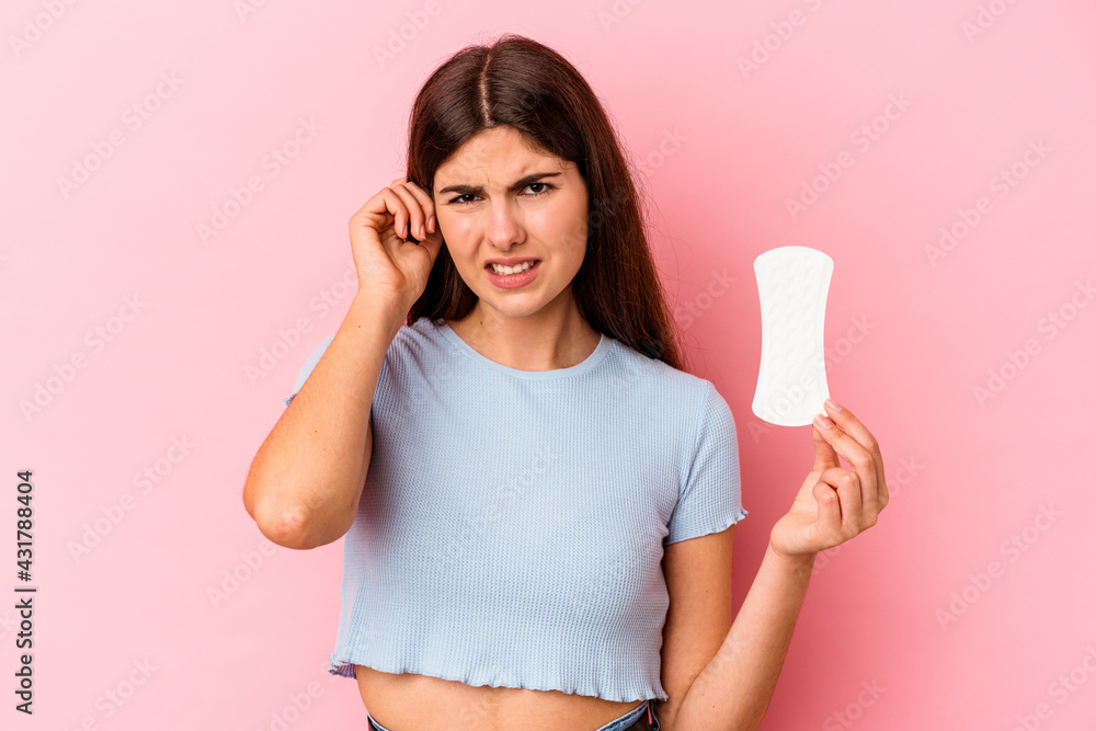 Young caucasian woman holding a compress isolated on pink background covering ears with hands. Young caucasian woman holding a compress isolated on pink background covering ears with hands.
