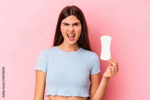 Young caucasian woman holding a compress isolated on pink background screaming very angry and aggressive.