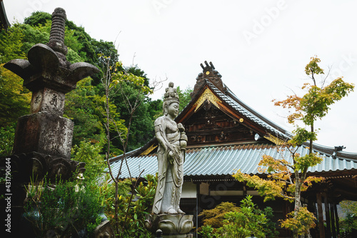 Buddhist statue between shrines and trees at Daisho-in temple with golden decorated roof in Miyajima, Hiroshima, Japan photo