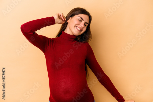 Young caucasian pregnant woman isolated on beige background dancing and having fun.