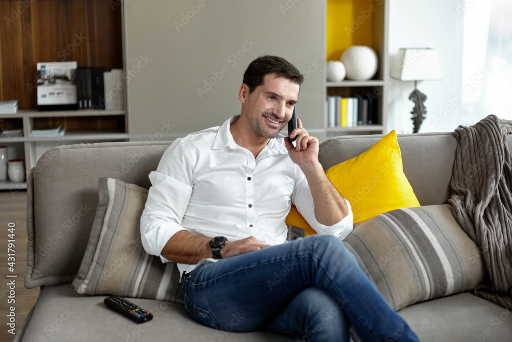 Portrait of a smiling young man sits on the couch comfortably holding a stationary phone.