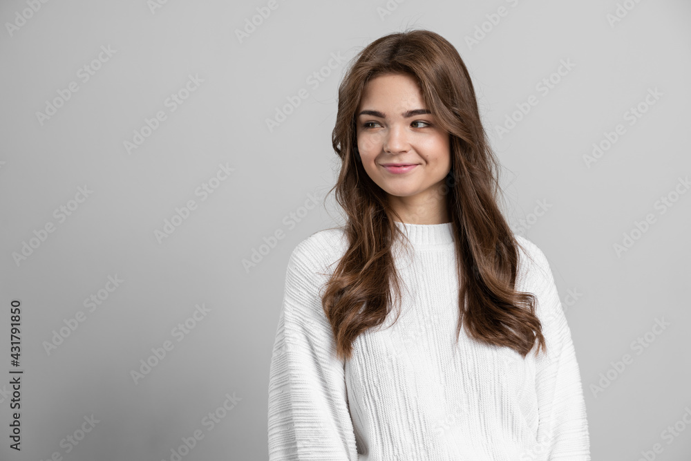 Attractive, young girl looks away on a gray background. Brunette on a blank wall background.