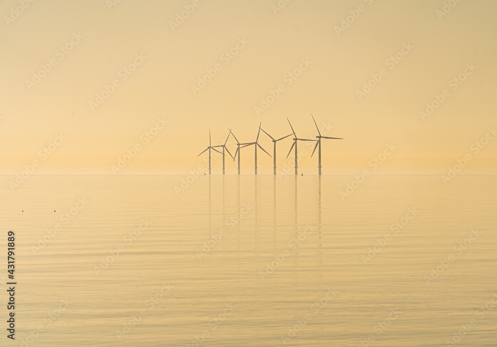 Offshore wind turbines generating renewable electricity and energy off the Essex clacton coast for eco backdrop, texture, wallpaper shiloutted against clear sky background