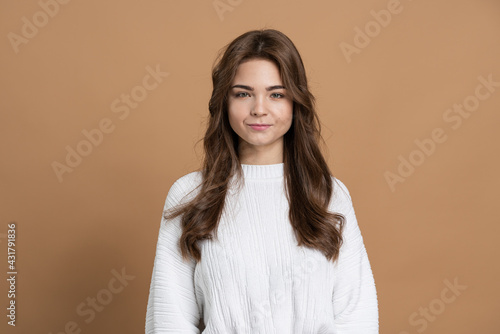 Attractive young girl with brown hair on a brown background. Beautiful girl isolated on a blank wall