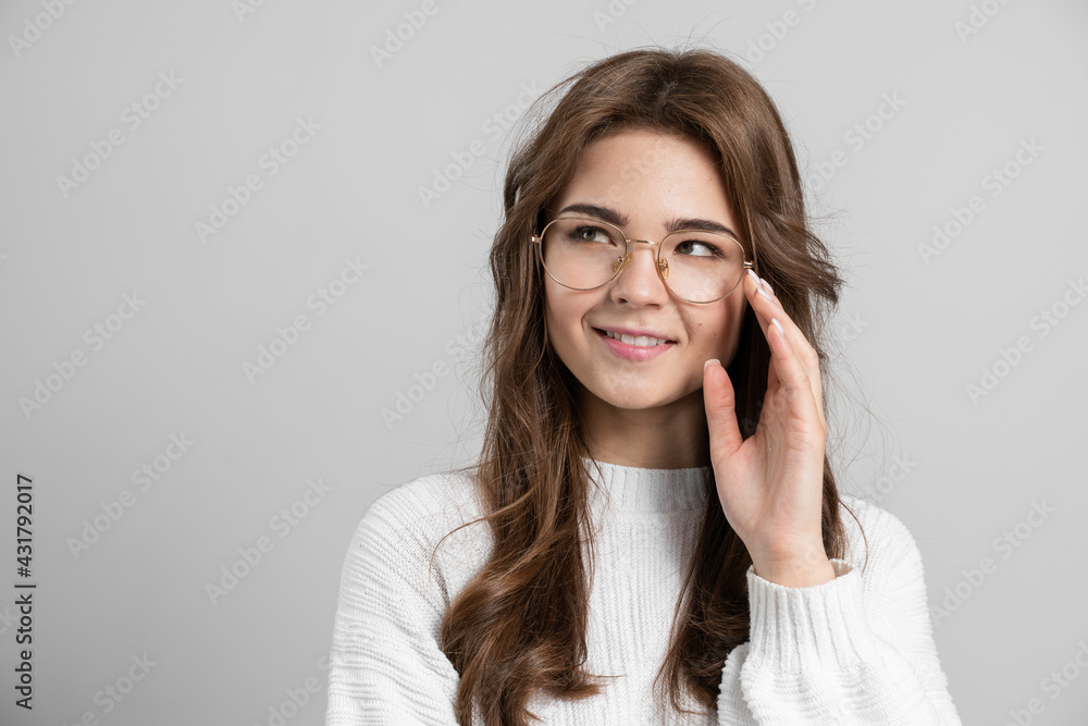Young, cute woman, wearing glasses, looking away. On a gray background, a girl posing, looking at a copy space Young, cute woman, wearing glasses, looking away. On a gray background, a girl posing, looking at a copy space