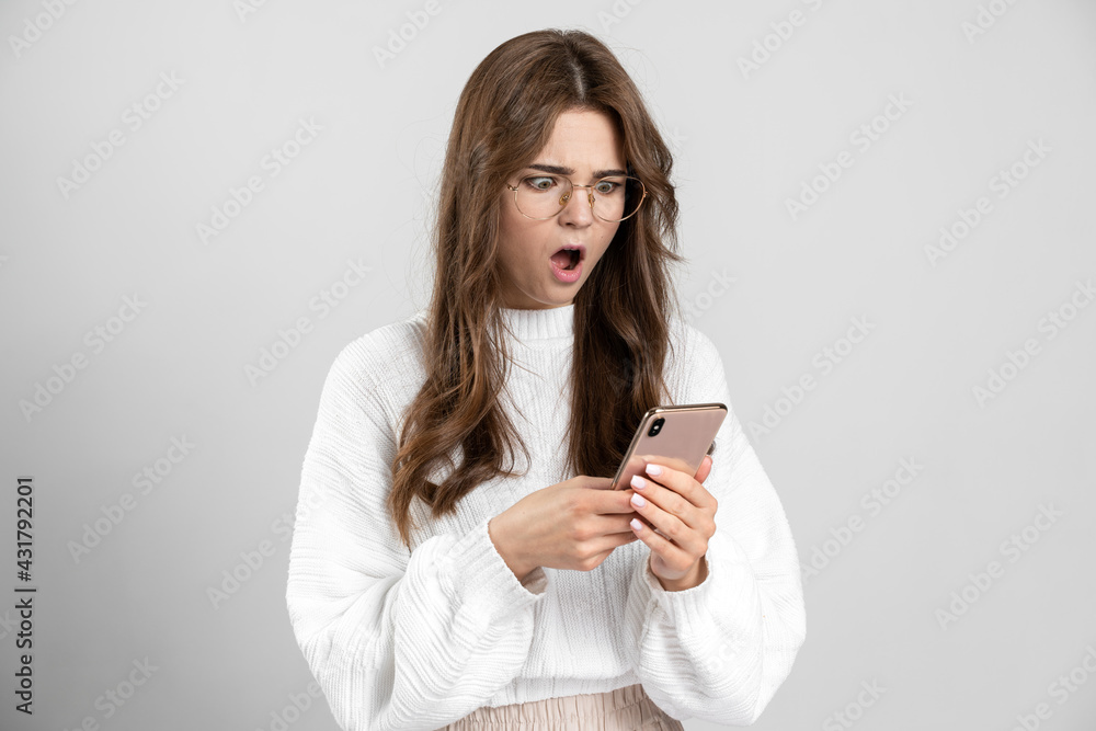 Surprised, pretty girl is very surprised, looking at a mobile phone. The charming girl in glasses is shocked by what she saw in her phone. Surprised, pretty girl is very surprised, looking at a mobile phone. The charming girl in glasses is shocked by what she saw in her phone.
