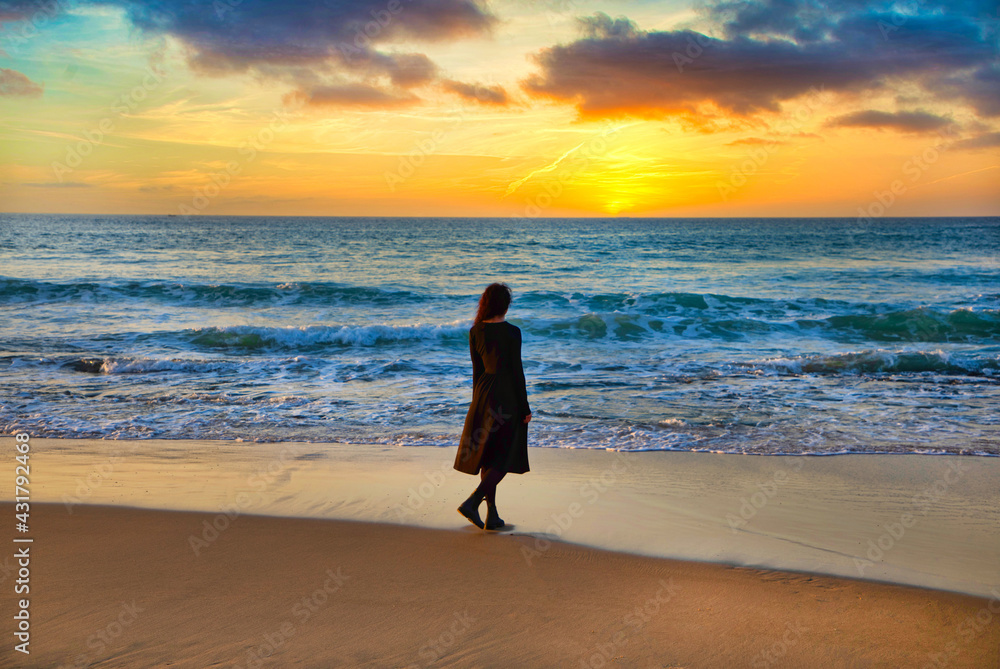 a young girl stands on the shore and looks at the sea at sunset