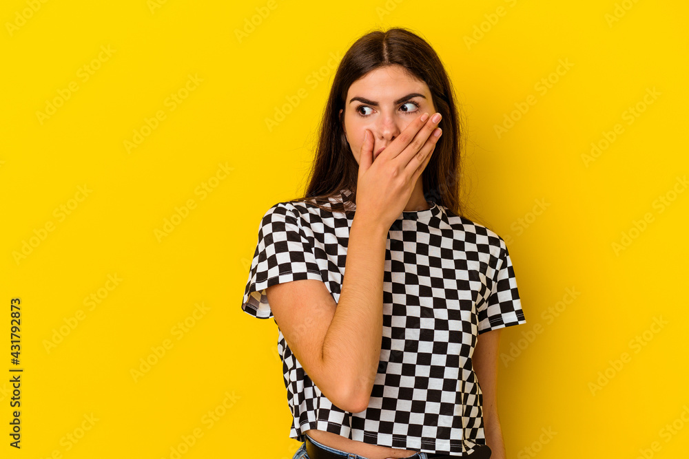 Young caucasian woman isolated on yellow background thoughtful looking to a copy space covering mouth with hand. Young caucasian woman isolated on yellow background thoughtful looking to a copy space covering mouth with hand.