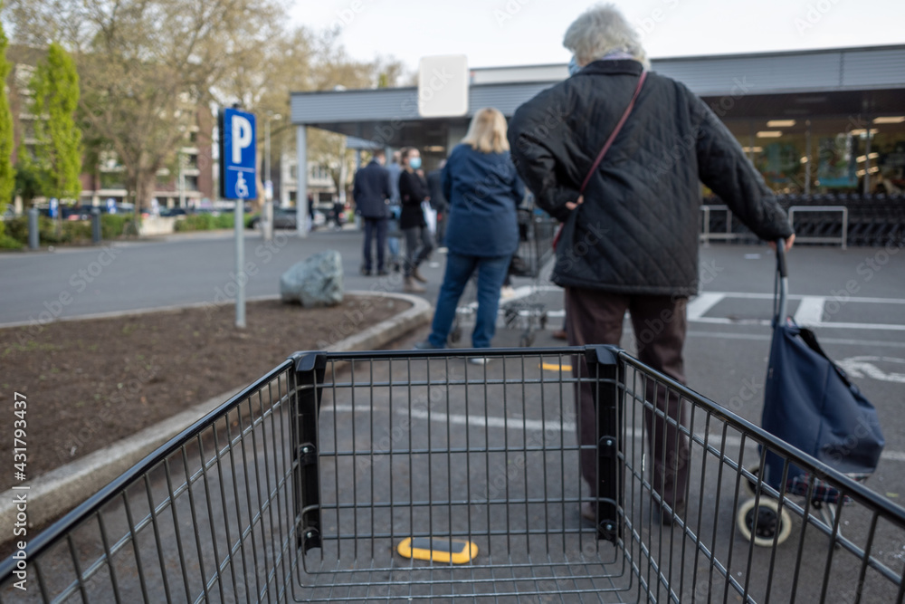 Selective focus at shopping cart, European people queue on street outside supermarket during lockdown during epidemic COVID-19 virus in Düsseldorf, Germany.