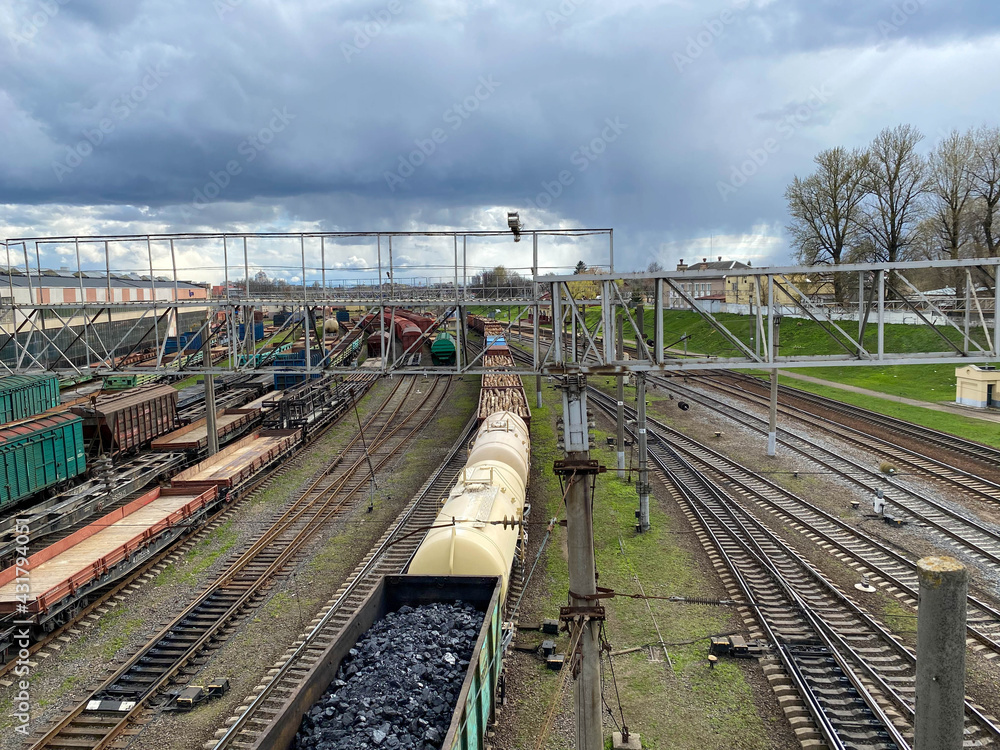 Aerial view of colorful freight trains on railway station. Wagons with goods on railroad. Cargo trains. Heavy industry. Industrial scene with trains, city buildings and blue sky at sunset. Top view Aerial view of colorful freight trains on railway station. Wagons with goods on railroad. Cargo trains. Heavy industry. Industrial scene with trains, city buildings and blue sky at sunset. Top view