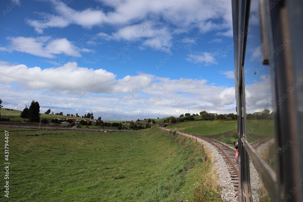 Amazing train travel in Ecuador South America between green fields with a beautiful reflection of the railroad in the train window and a blue cloudy sky in the background