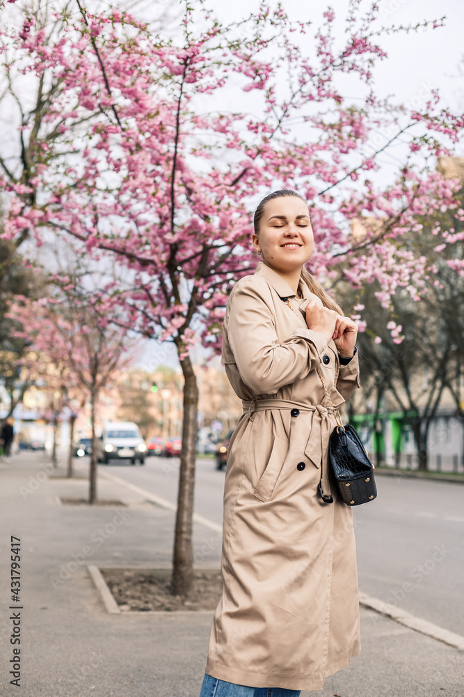 Beautiful woman near sakura trees. Pink flowers bloom in the trees on a city street. Trees bloom around. Spring time concept Beautiful woman near sakura trees. Pink flowers bloom in the trees on a city street. Trees bloom around. Spring time concept