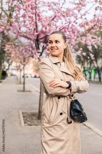 Beautiful woman near sakura trees. Pink flowers bloom in the trees on a city street. Trees bloom around. Spring time concept