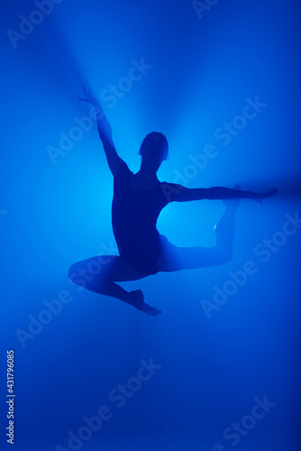 Professional ballerina dancing ballet in smoke. Female in black bodysuit on floodlights background.