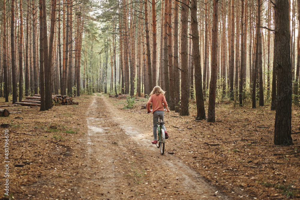 Caucasian teenage girl faceless on a bicycle rides in the forest. Relaxation and wellness concept.
