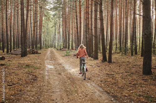 Caucasian teenage girl faceless on a bicycle rides in the forest. Relaxation and wellness concept.