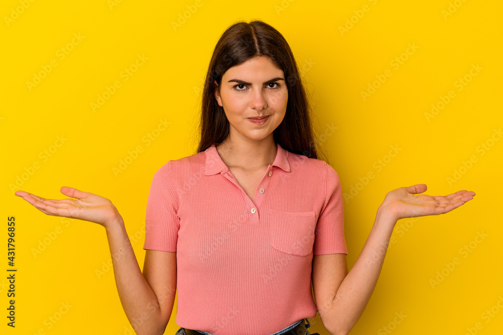 Young caucasian woman isolated on yellow background confused and doubtful shrugging shoulders to hold a copy space. Young caucasian woman isolated on yellow background confused and doubtful shrugging shoulders to hold a copy space.