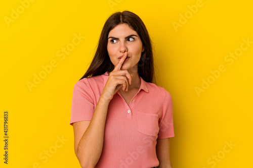 Young caucasian woman isolated on yellow background keeping a secret or asking for silence.