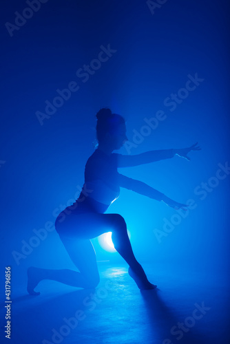 Professional ballerina dancing ballet in smoke. Female in black bodysuit on floodlights background. © Ivan Zelenin