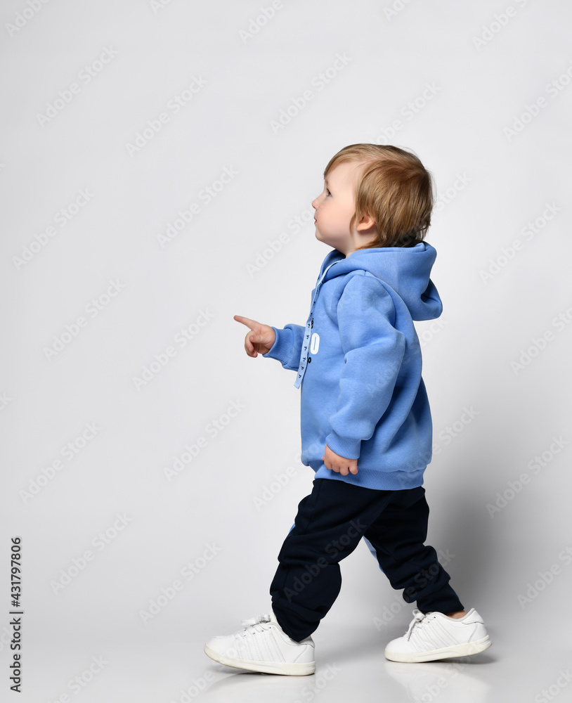 toddler in a warm blue hoodie and wide sweatpants walks to the side and shows something toddler in a warm blue hoodie and wide sweatpants walks to the side and shows something