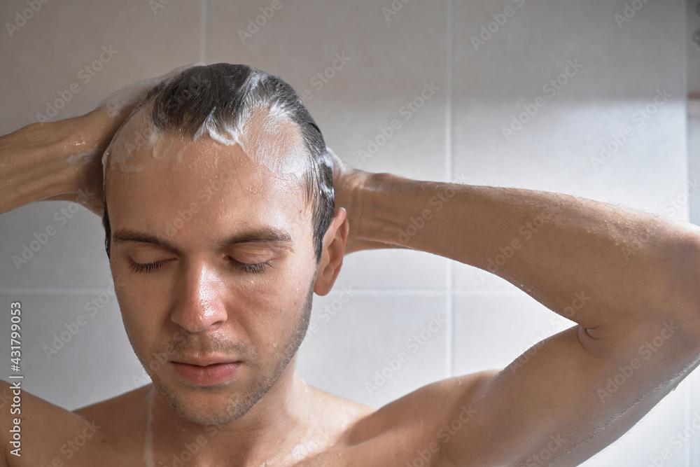 Portrait of young handsome man washes himself with shower gel, lathers head with shampoo in the bathroom at home close-up Portrait of young handsome man washes himself with shower gel, lathers head with shampoo in the bathroom at home close-up