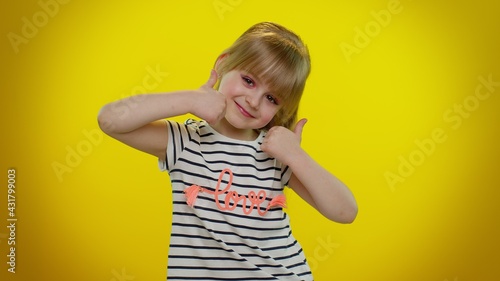 Girl raises thumbs up. Little blonde teen kid child agrees with something, gives positive reply recommends advertisement likes good posing isolated on yellow studio background. Young children emotion