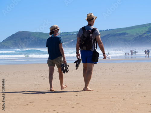 Pareja de hombre y mujer jóvenes, paseando con  sombreo y pantalón corto  por la playa del Merón en las vacaciones del verano de 2020 en Santander, España.