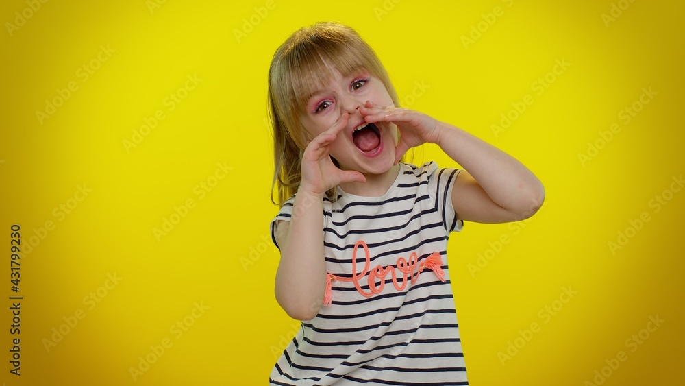 Hey you. Little blonde teen kid child girl in striped t-shirt shouting hello, waving hand, welcoming with hi gesture. Posing isolated on yellow studio background. Young children lifestyle emotions Hey you. Little blonde teen kid child girl in striped t-shirt shouting hello, waving hand, welcoming with hi gesture. Posing isolated on yellow studio background. Young children lifestyle emotions