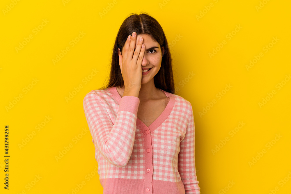Young caucasian woman isolated on yellow background having fun covering half of face with palm.