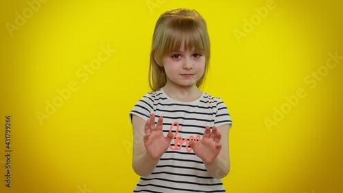 Hey you, be careful. Cute kid child girl 5-6 years old warning with admonishing finger gesture, saying no, scolding and giving advice to avoid danger, disapproval sign on yellow studio wall background