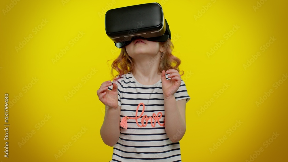 Little teen child kid girl using virtual reality futuristic technology VR  app headset helmet to play simulation 3D 360 video game, drawing. Young  children posing isolated on yellow studio background foto de