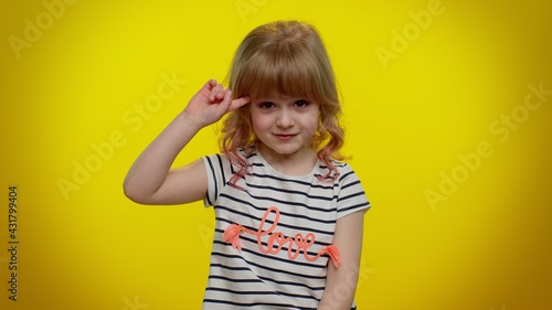 You are crazy, out of mind. Funny blonde kid child 5-6 years old pointing at camera and showing stupid gesture, blaming some idiot for insane plan. Teenager children girl on yellow studio background