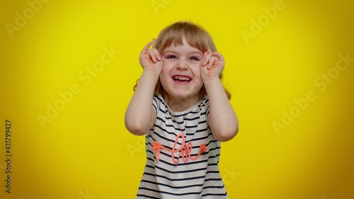 Little bit crazy funny playful blonde kid child 5-6 years old demonstrating tongue out, fooling around, making silly faces, madness. Lovely teenager children girl emotions on yellow studio background