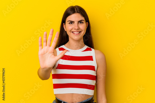 Young caucasian woman isolated on yellow background smiling cheerful showing number five with fingers. © Asier