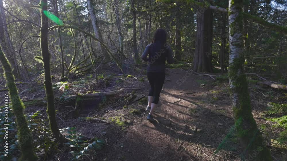 Caucasian Woman Trail Running in the Green Forest surrounded by beautiful trees. Taken in Squamish, British Columbia, Canada. Caucasian Woman Trail Running in the Green Forest surrounded by beautiful trees. Taken in Squamish, British Columbia, Canada.