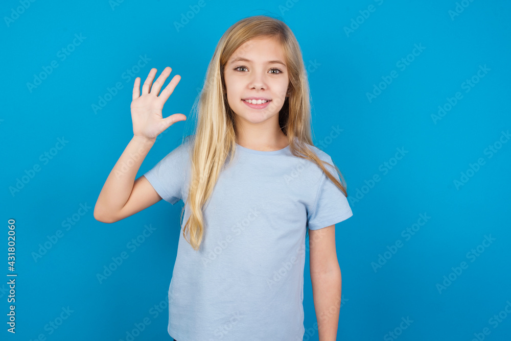 Fototapeta premium beautiful Caucasian little girl wearing blue T-shirt over blue background showing and pointing up with fingers number five while smiling confident and happy.