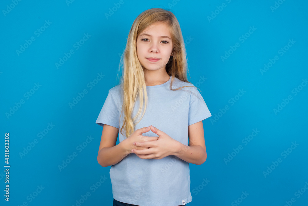 Business Concept - Portrait of beautiful Caucasian little girl wearing blue T-shirt over blue background holding hands with confident face. Business Concept - Portrait of beautiful Caucasian little girl wearing blue T-shirt over blue background holding hands with confident face.