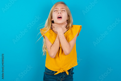 Photos Caucasian kid girl wearing yellow T-shirt against blue wall shouting suffocate because painful strangle
