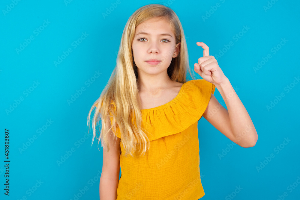 Caucasian kid girl wearing yellow T-shirt against blue wall pointing up with fingers number nine in Chinese sign language Jiu Caucasian kid girl wearing yellow T-shirt against blue wall pointing up with fingers number nine in Chinese sign language Jiu