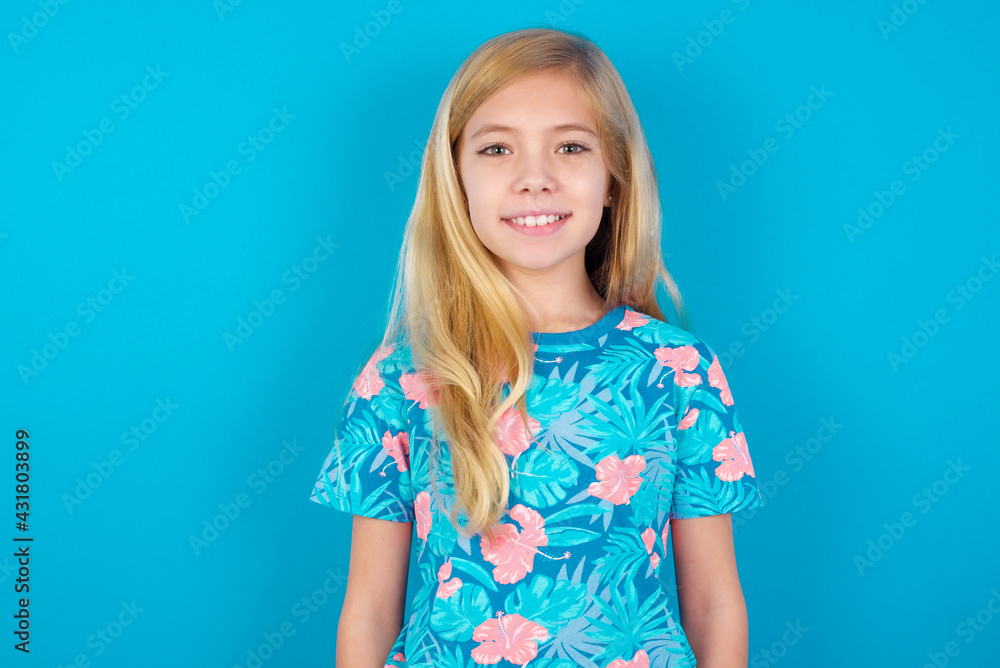Caucasian kid girl wearing hawaiian T-shirt against blue wall with nice beaming smile pleased expression. Positive emotions concept Caucasian kid girl wearing hawaiian T-shirt against blue wall with nice beaming smile pleased expression. Positive emotions concept