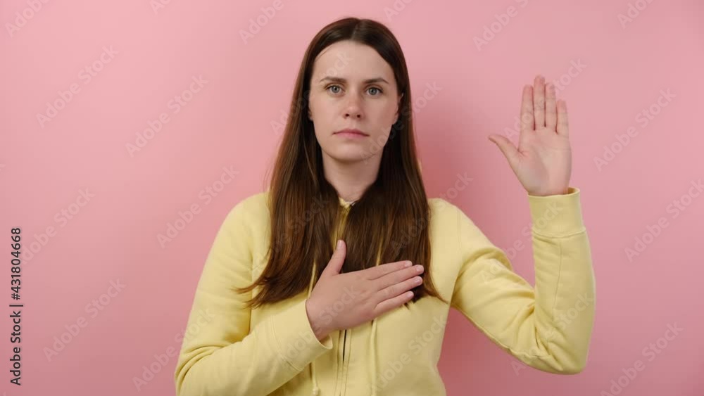 I swear. Honest truthful young caucasian woman making loyalty promise oath, keeps hand on chest, gestures with palm, promises something, wears yellow hoodie, isolated over pink studio background wall I swear. Honest truthful young caucasian woman making loyalty promise oath, keeps hand on chest, gestures with palm, promises something, wears yellow hoodie, isolated over pink studio background wall