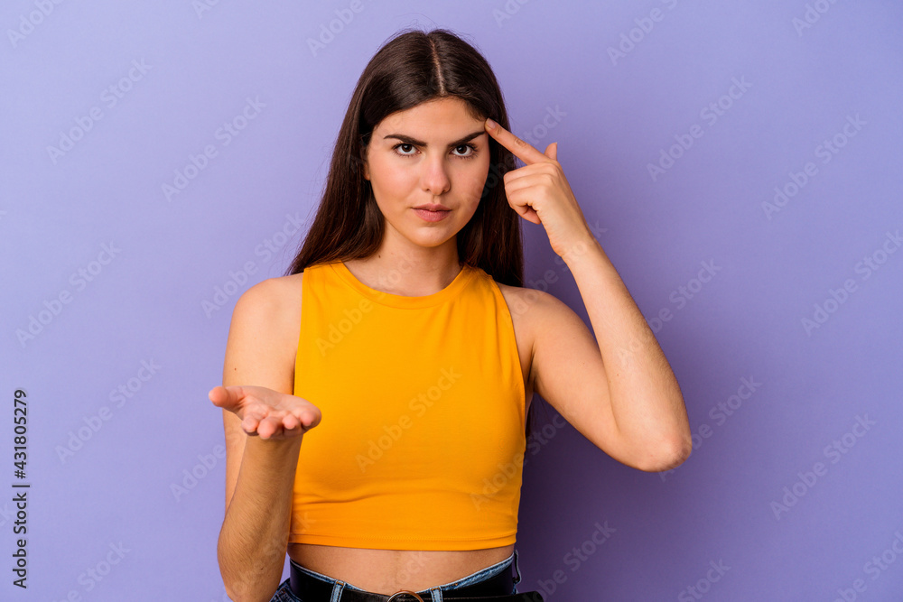 Young caucasian woman isolated on purple background holding and showing a product on hand. Young caucasian woman isolated on purple background holding and showing a product on hand.