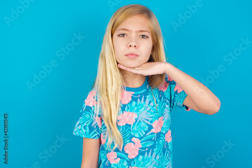 Caucasian kid girl wearing hawaiian T-shirt against blue wall cutting throat with hand as knife, threaten aggression with furious violence.