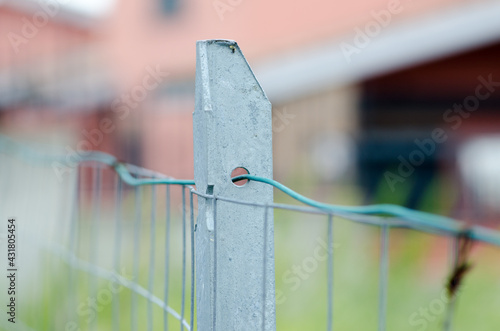 Fence post, in galvanized stainless steel, with blurred wires and mesh